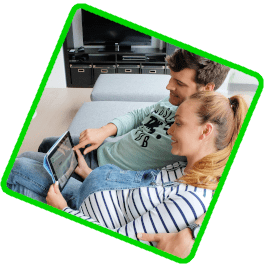 Les deux personnes de ce jeune couple sont assises dans le fauteuil. À l'aide de leur tablette, ils commandent leur espace d’entreposage en ligne sur le site Internet de Box@Home.